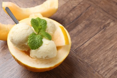 Scoops of tasty melon sorbet with mint in fresh fruit on wooden table, closeup. Space for text