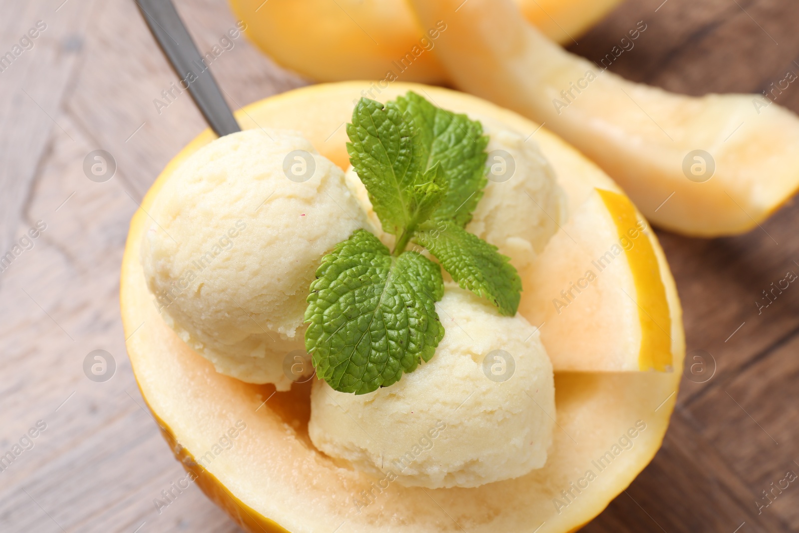 Photo of Scoops of tasty melon sorbet with mint in fresh fruit on wooden table, closeup