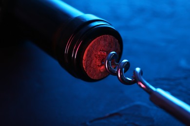 Photo of Wine bottle with corkscrew in lights on table, closeup