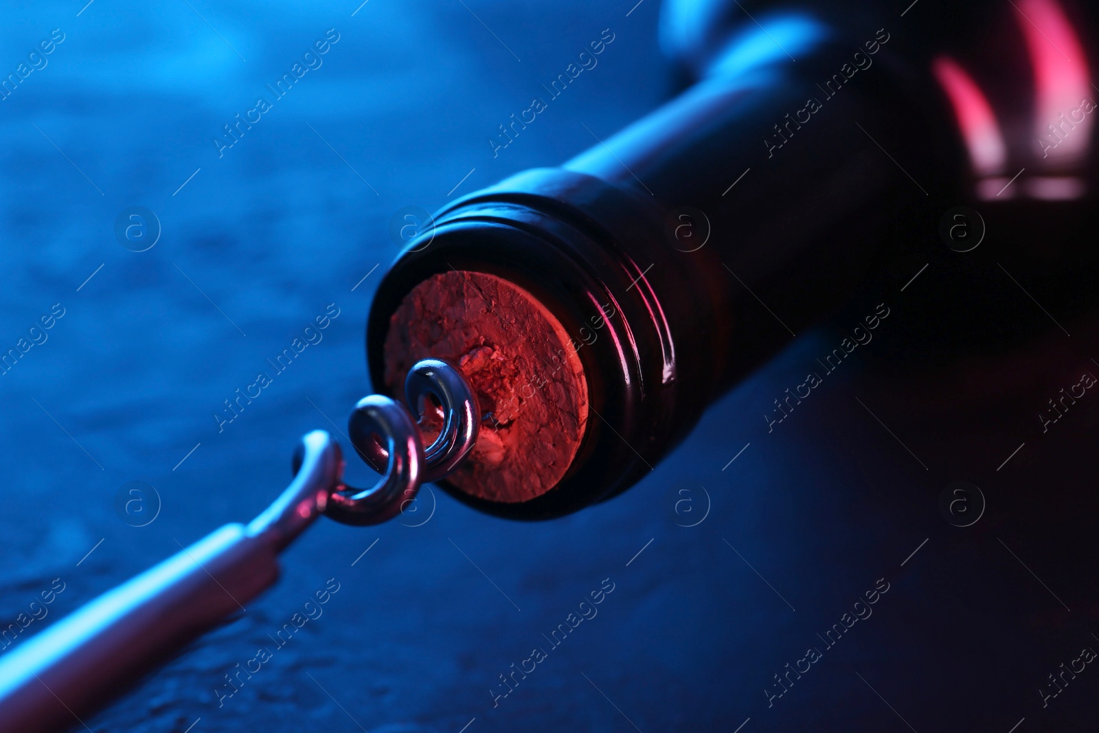 Photo of Wine bottle with corkscrew in lights on table, closeup