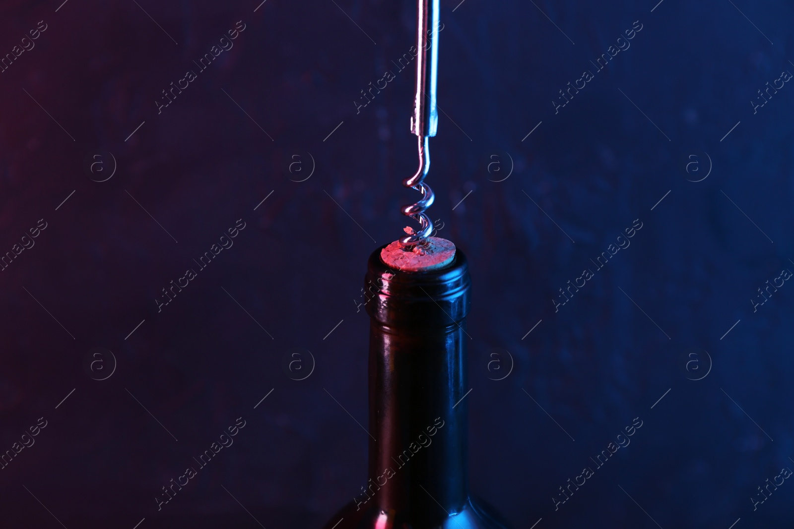 Photo of Wine bottle with corkscrew in lights on dark background, closeup