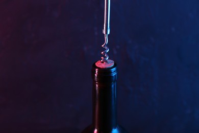 Photo of Wine bottle with corkscrew in lights on dark background, closeup