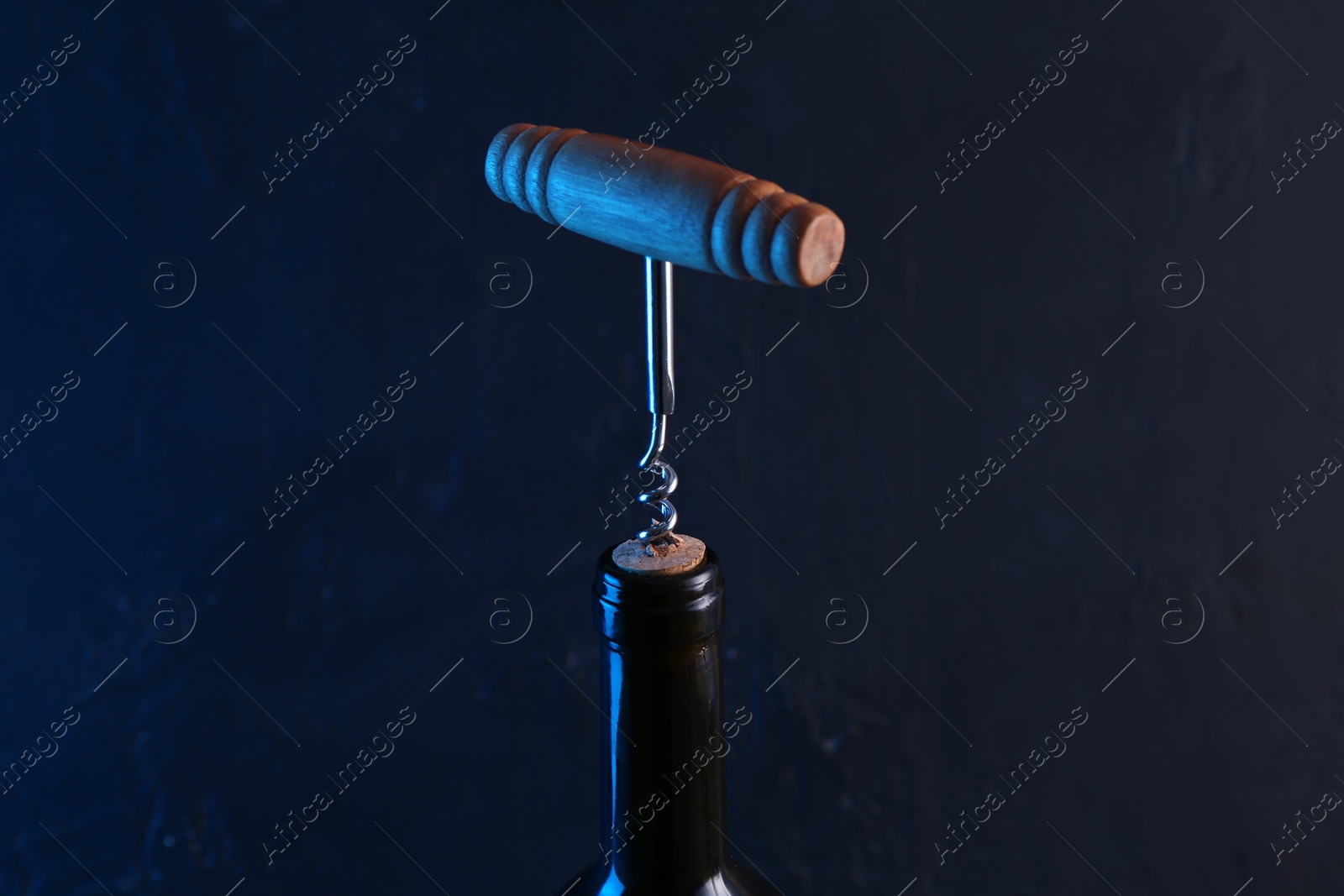 Photo of Wine bottle with corkscrew on dark background, closeup