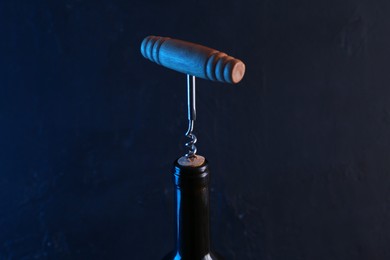 Photo of Wine bottle with corkscrew on dark background, closeup