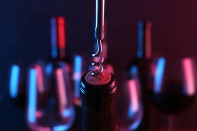 Photo of Wine bottle with corkscrew in lights on blurred background, closeup