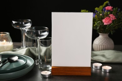 Photo of Menu holder, clean dishware and burning candles on grey table against black background