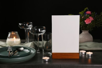 Photo of Menu holder, clean dishware and burning candles on grey table against black background