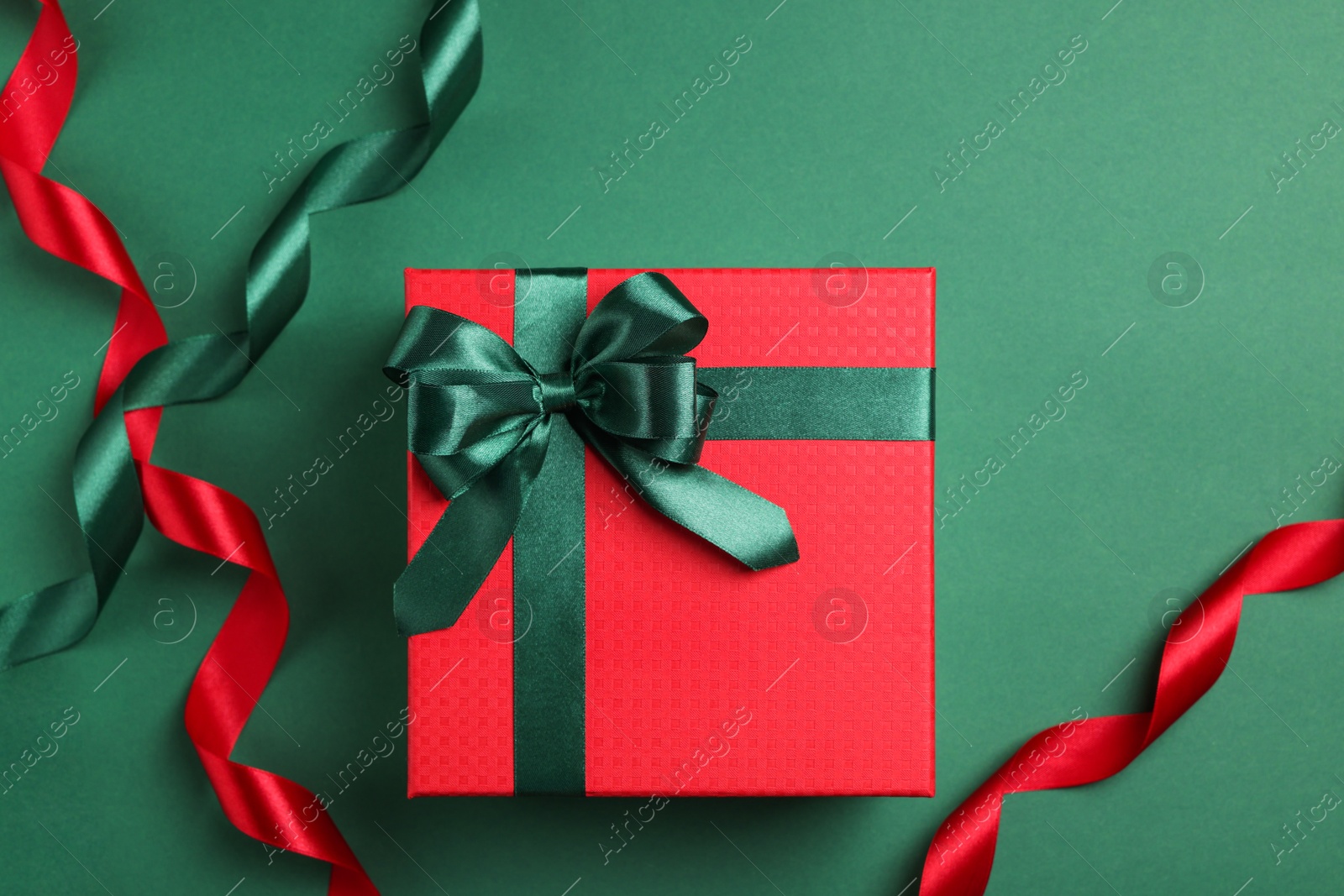 Photo of Beautiful red gift box with bright bow and ribbons on green background, flat lay