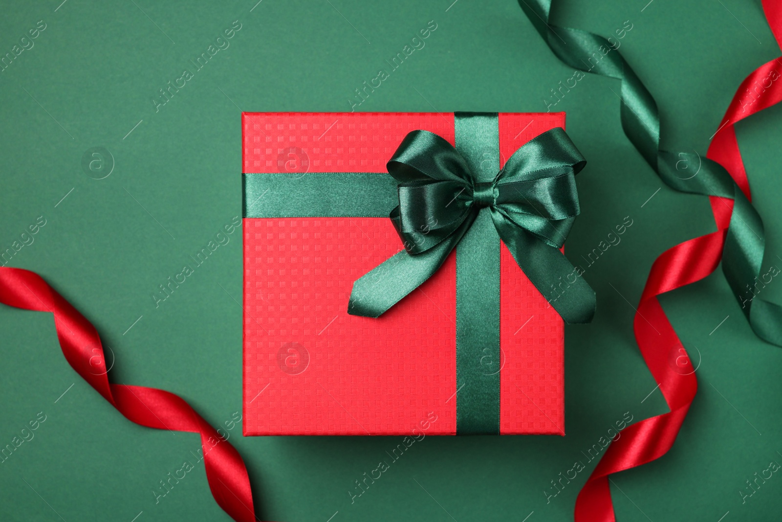 Photo of Beautiful red gift box with bright bow and ribbons on green background, flat lay