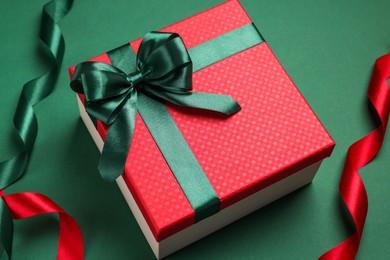 Photo of Beautiful red gift box with bright bow and ribbons on green background