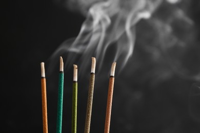 Aromatic incense sticks smoldering on black background