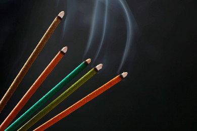 Photo of Aromatic incense sticks smoldering on black background