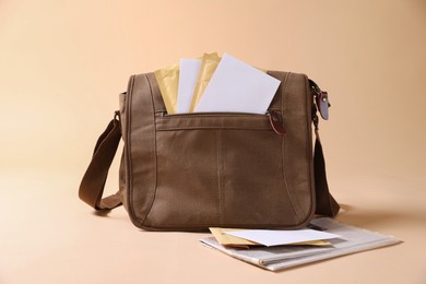 Photo of Brown postman's bag with envelopes and newspapers on beige background