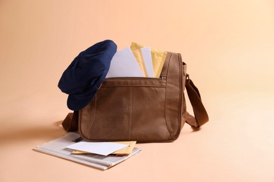 Brown postman's bag, envelopes, newspapers and hat on beige background