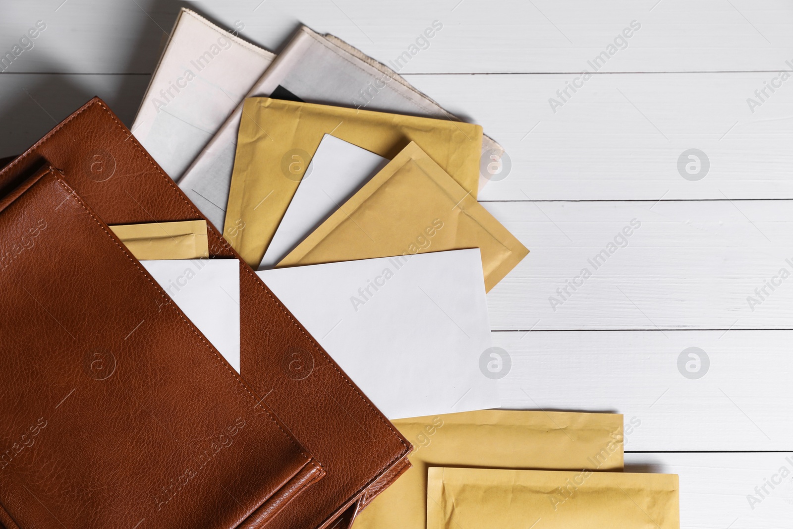 Photo of Brown postman's bag with envelopes and newspapers on white wooden table, top view. Space for text