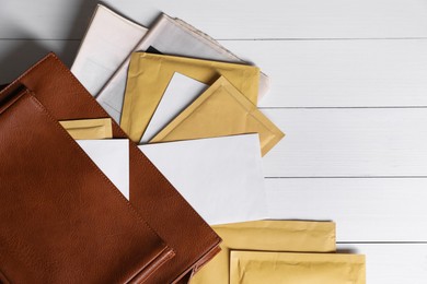 Brown postman's bag with envelopes and newspapers on white wooden table, top view. Space for text