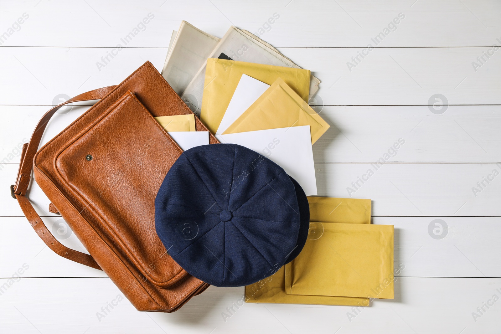 Photo of Brown postman's bag, envelopes, newspapers and hat on white wooden table, top view