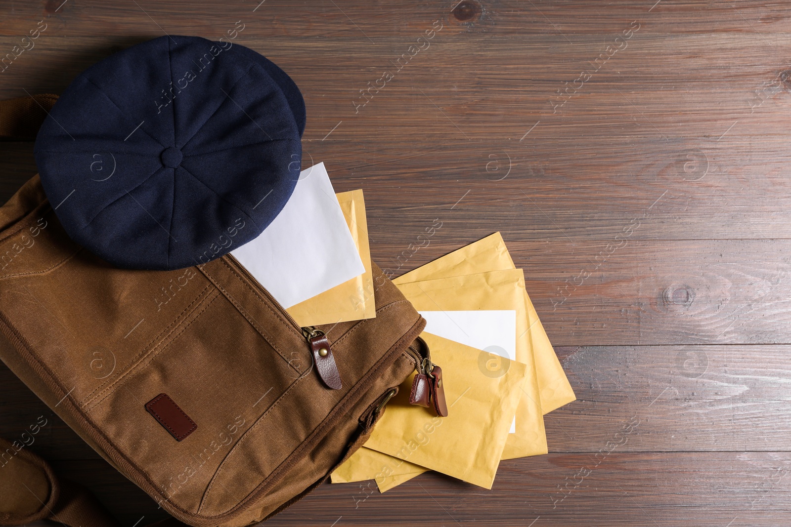 Photo of Brown postman's bag, envelopes, newspapers and hat on wooden table, top view. Space for text