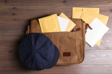 Photo of Brown postman's bag, envelopes, newspapers and hat on wooden table, top view