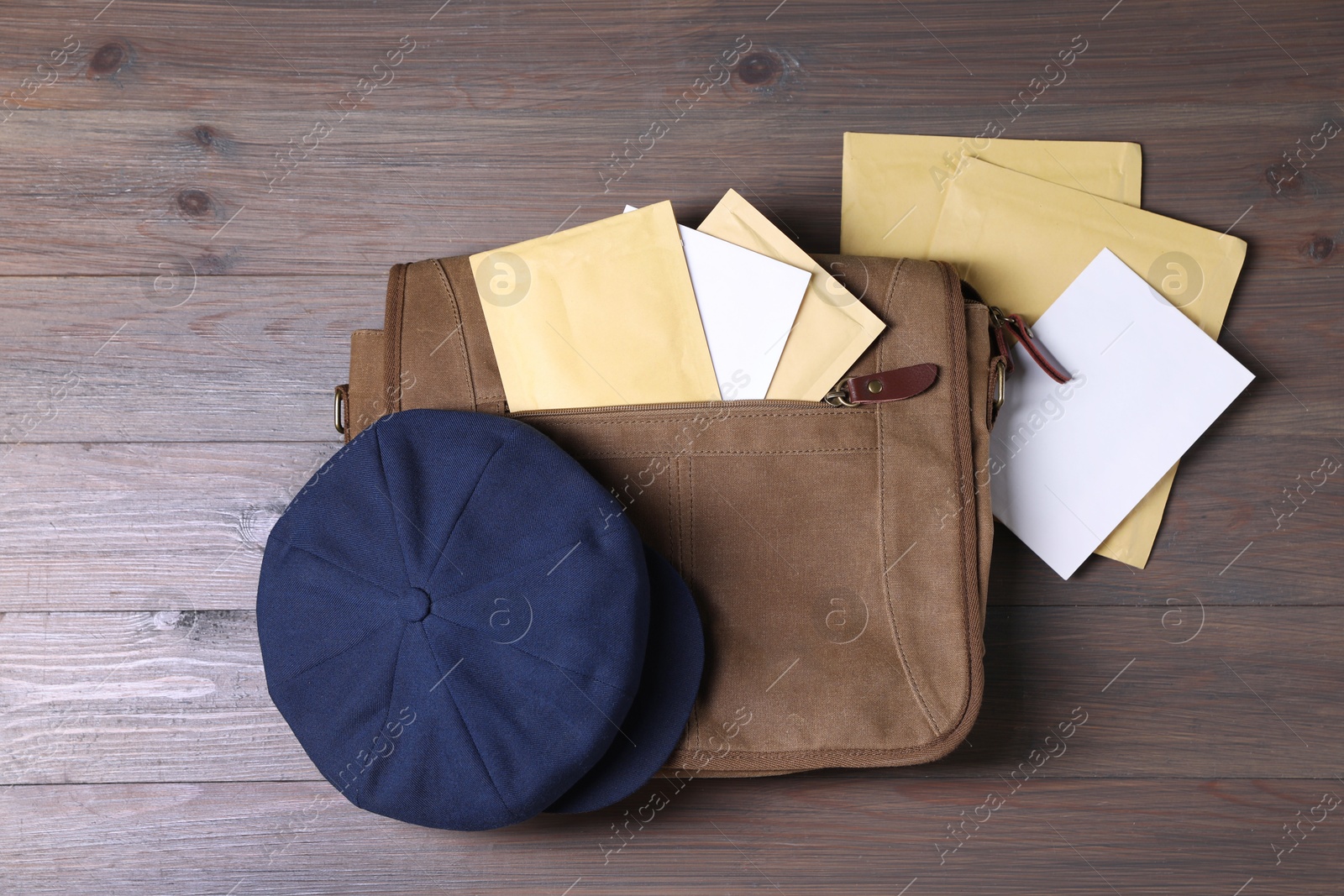 Photo of Brown postman's bag, envelopes, newspapers and hat on wooden table, top view