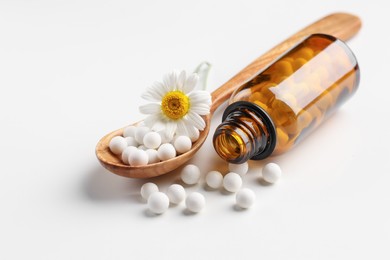 Homeopathic remedy. Spoon with pills, bottle and chamomile flower on white background