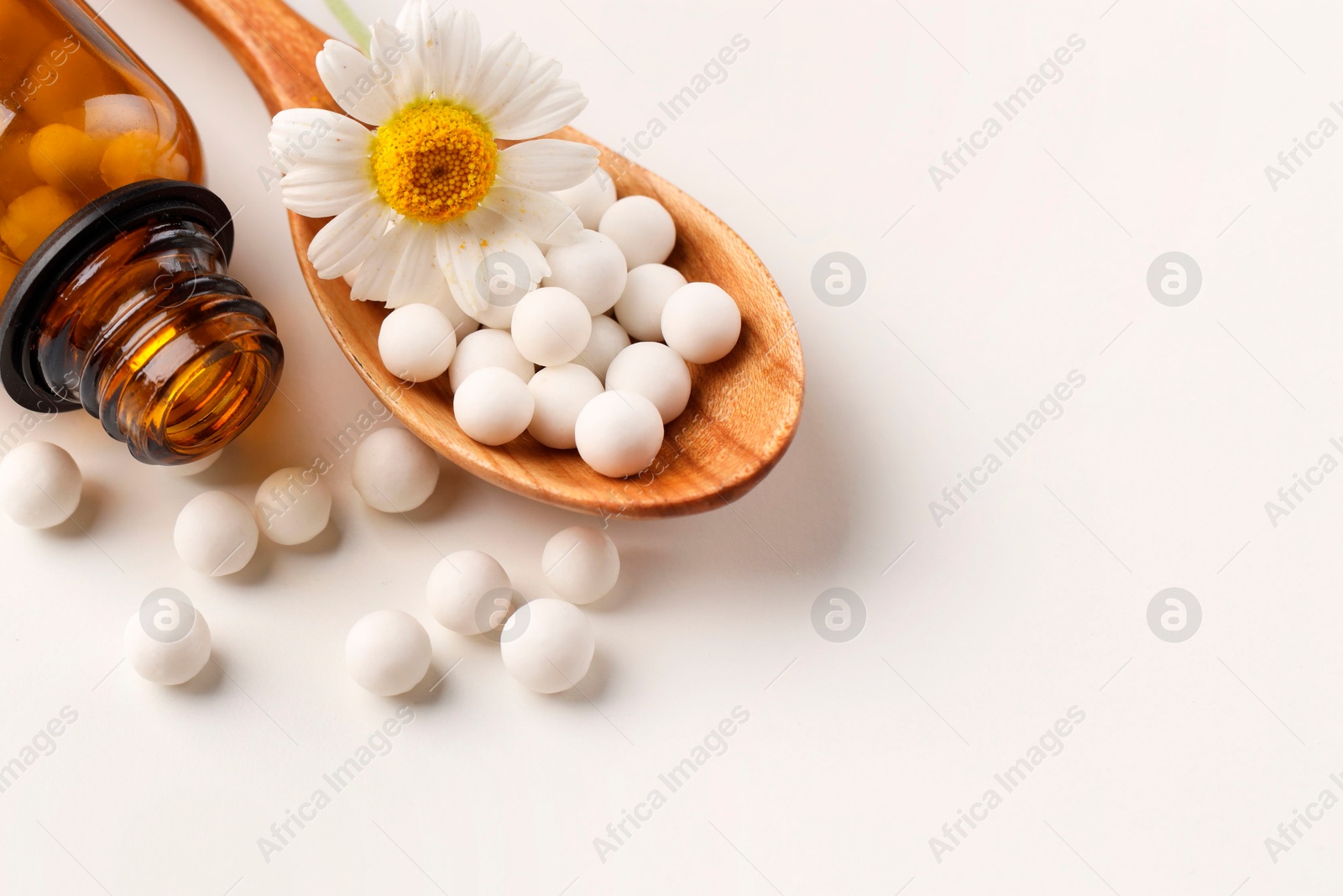 Photo of Homeopathic remedy. Spoon with pills, bottle and chamomile flower on white background. Space for text