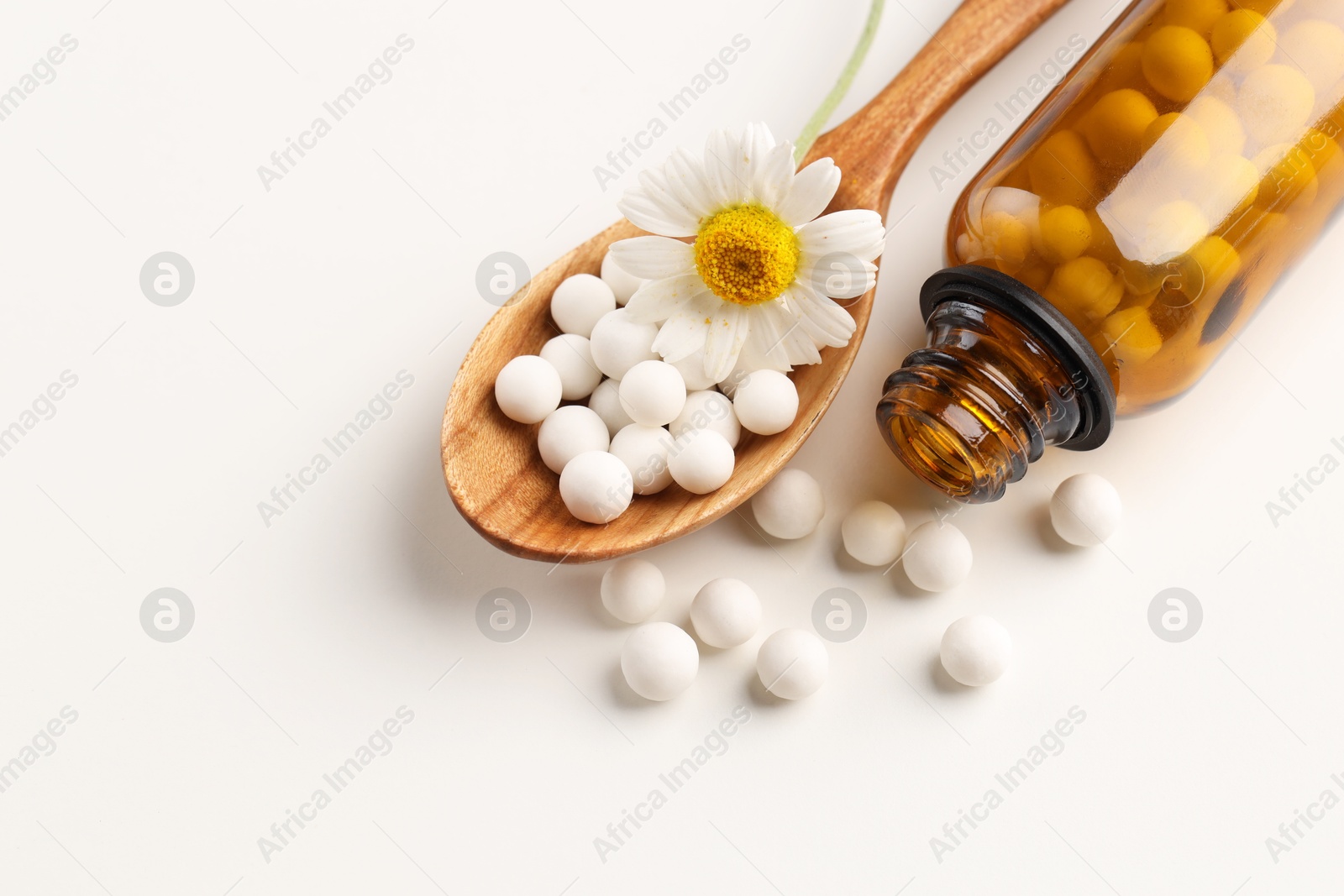 Photo of Homeopathic remedy. Spoon with pills, bottle and chamomile flower on white background, top view. Space for text