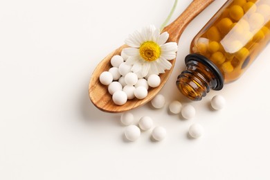 Homeopathic remedy. Spoon with pills, bottle and chamomile flower on white background, top view. Space for text