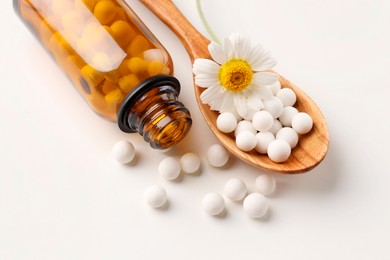 Homeopathic remedy. Spoon with pills, bottle and chamomile flower on white background