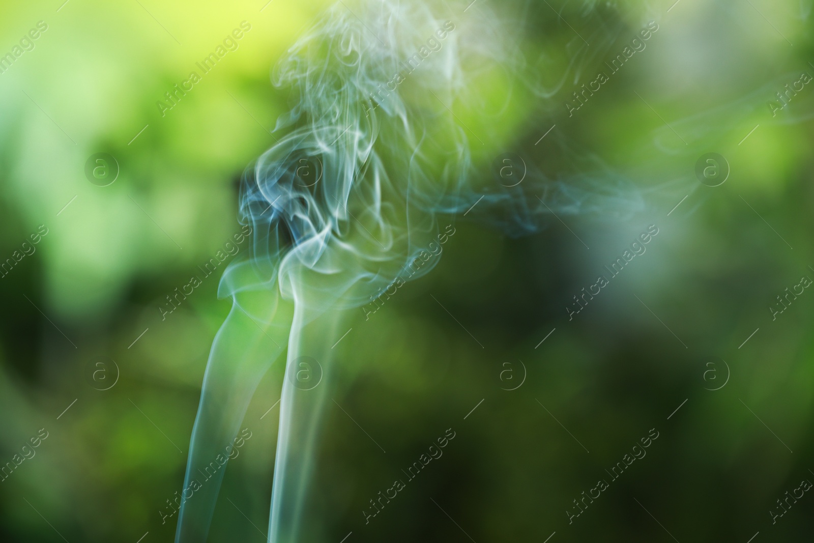 Photo of Smoke from incense stick on green blurred background, space for text