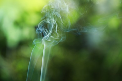 Smoke from incense stick on green blurred background, space for text