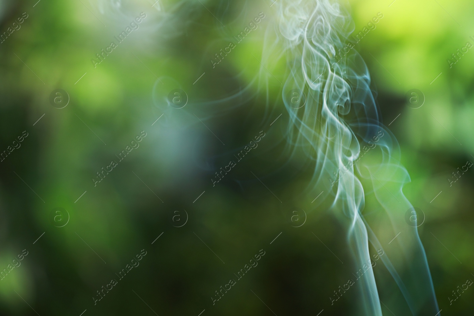 Photo of Smoke from incense stick on green blurred background, space for text