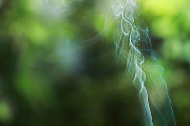 Photo of Smoke from incense stick on green blurred background, space for text