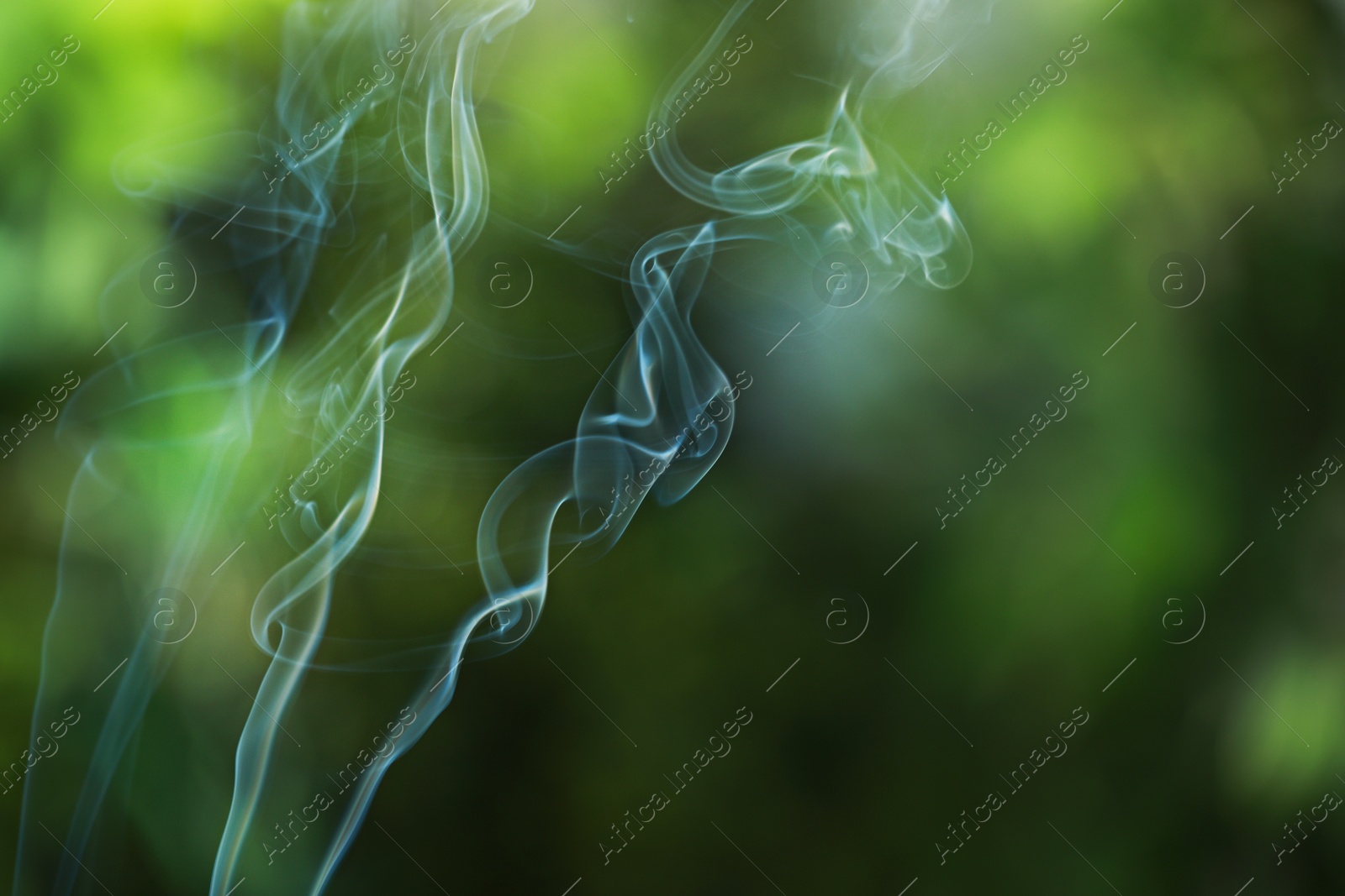 Photo of Smoke from incense stick on green blurred background, space for text