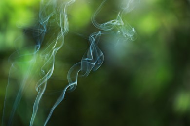 Smoke from incense stick on green blurred background, space for text