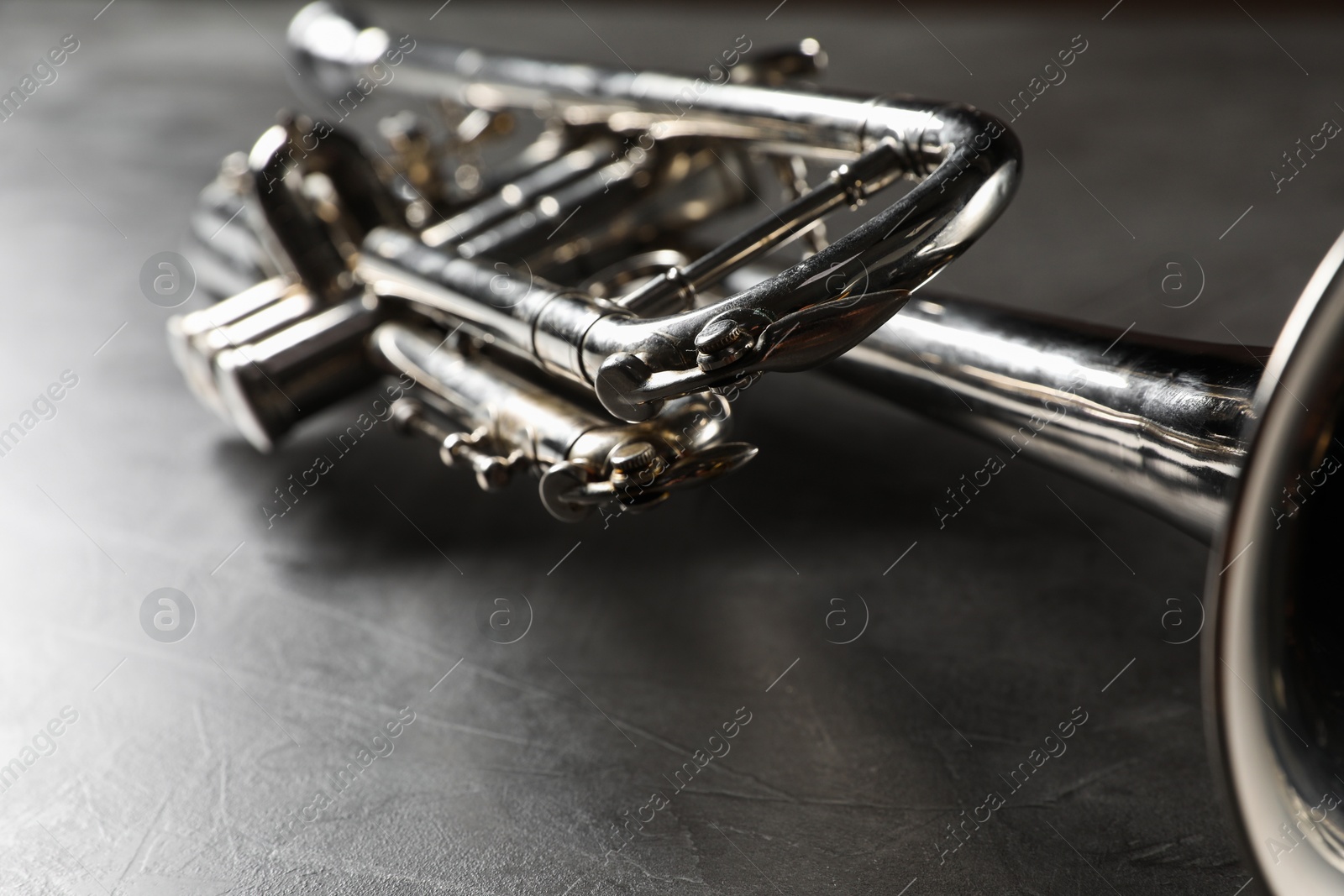 Photo of Closeup view of shiny trumpet on grey textured table. Wind musical instrument