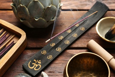 Photo of Incense stick smoldering in holder and Tibetan singing bowl on wooden table, closeup. Om ligature