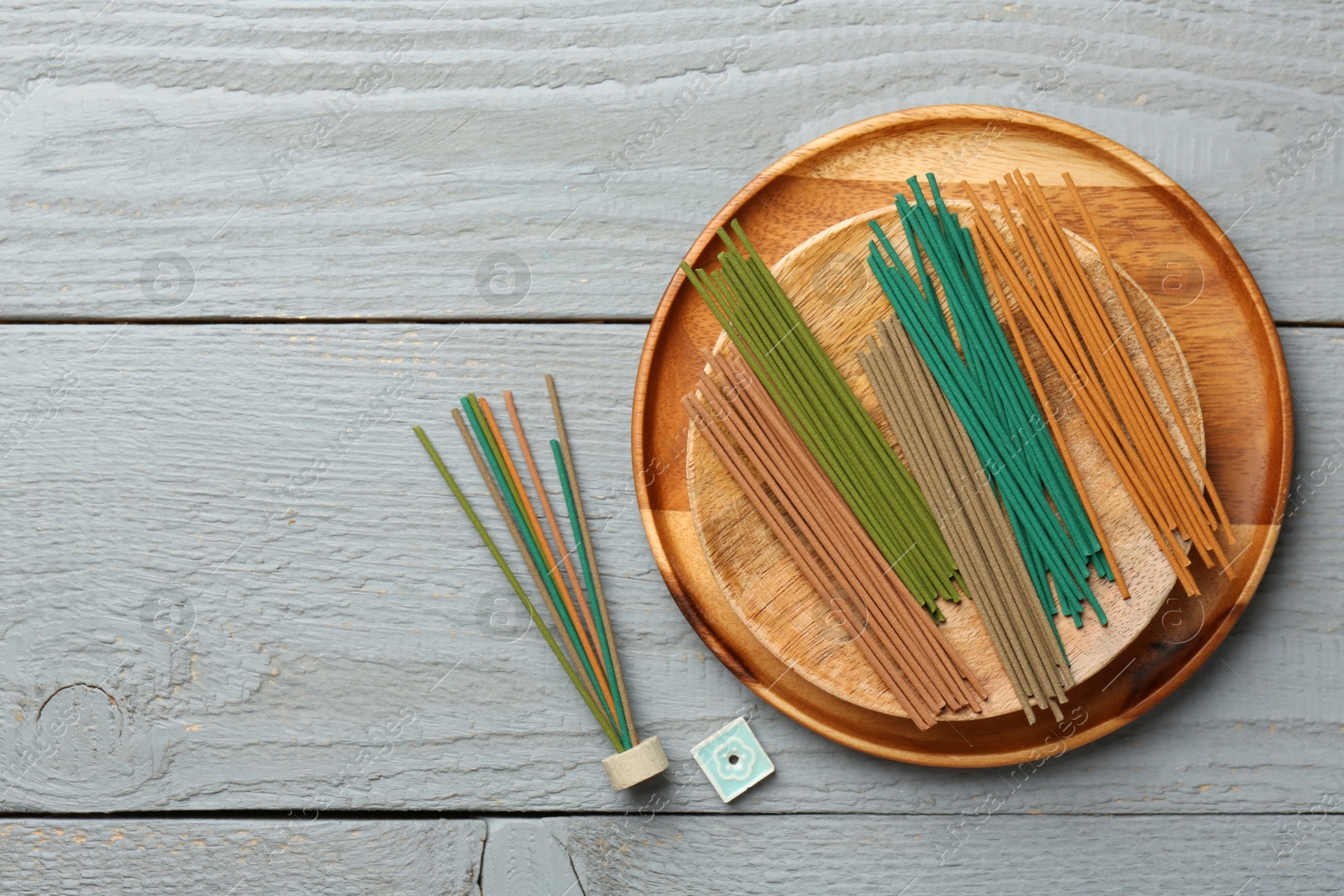 Photo of Incense sticks and small ceramic stand on gray wooden table, flat lay. Space for text