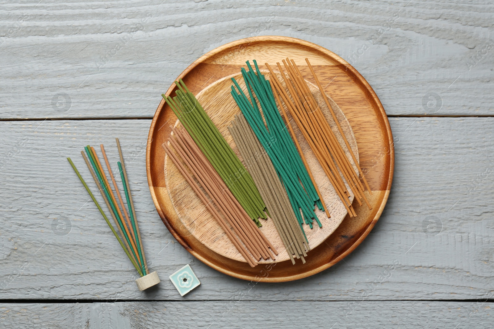 Photo of Incense sticks and small ceramic stand on gray wooden table, flat lay