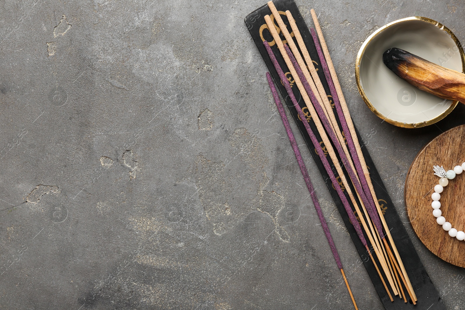 Photo of Incense sticks, holder, Santo Palo and bracelet on gray textured table, flat lay with space for text. Om ligature