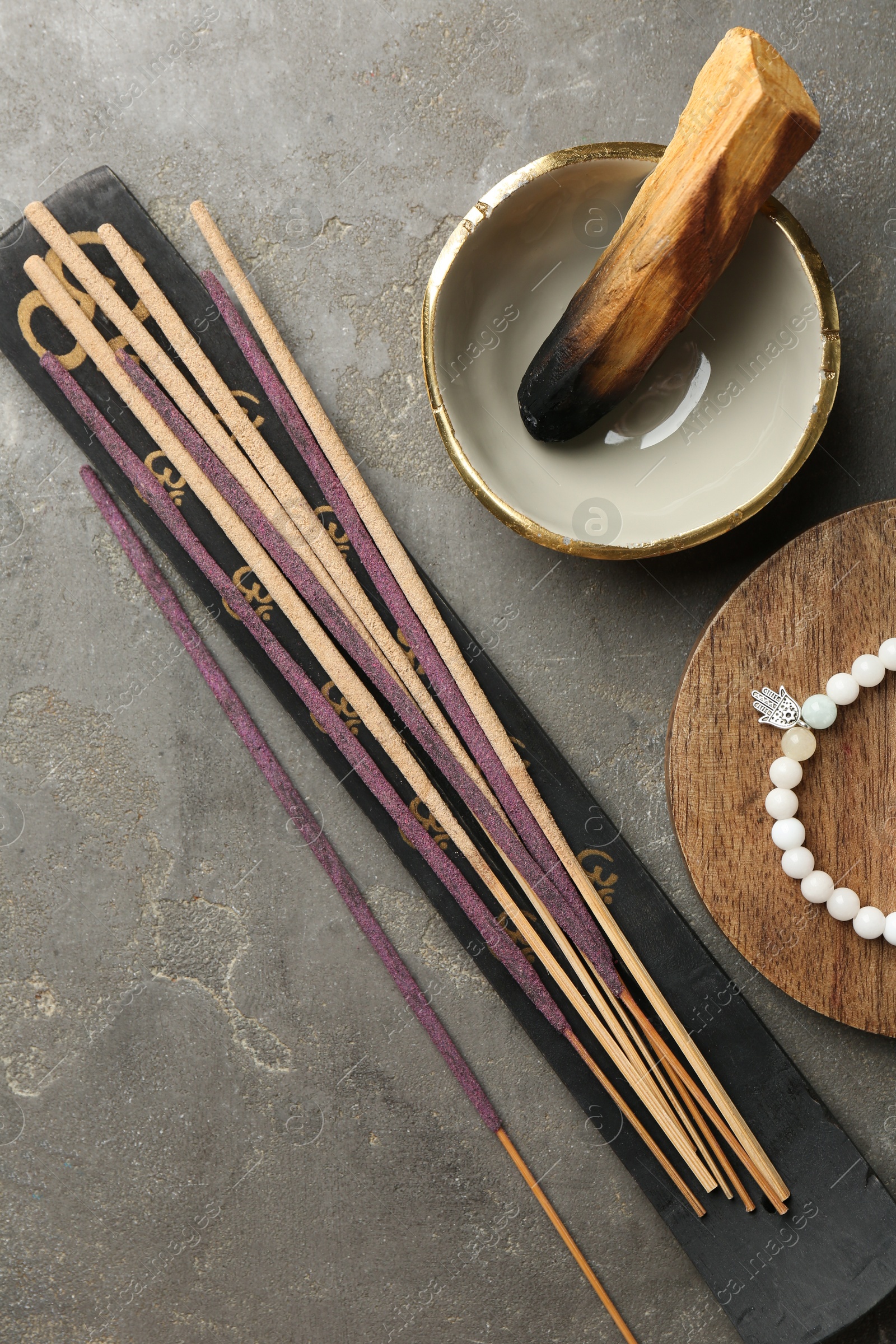 Photo of Incense sticks, holder, Santo Palo and bracelet on gray textured table, flat lay. Om ligature