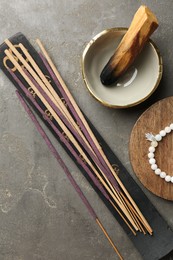 Photo of Incense sticks, holder, Santo Palo and bracelet on gray textured table, flat lay. Om ligature