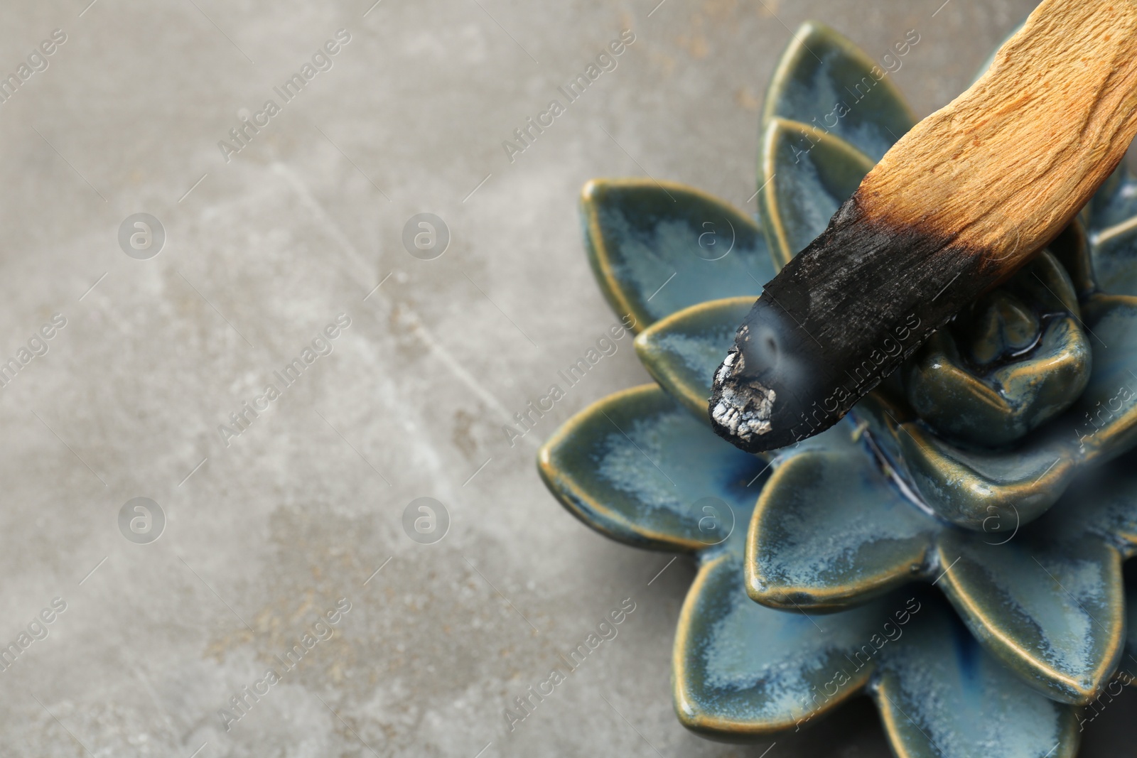 Photo of Smoldering Palo Santo stick and ceramic succulent on gray textured table, closeup. Space for text