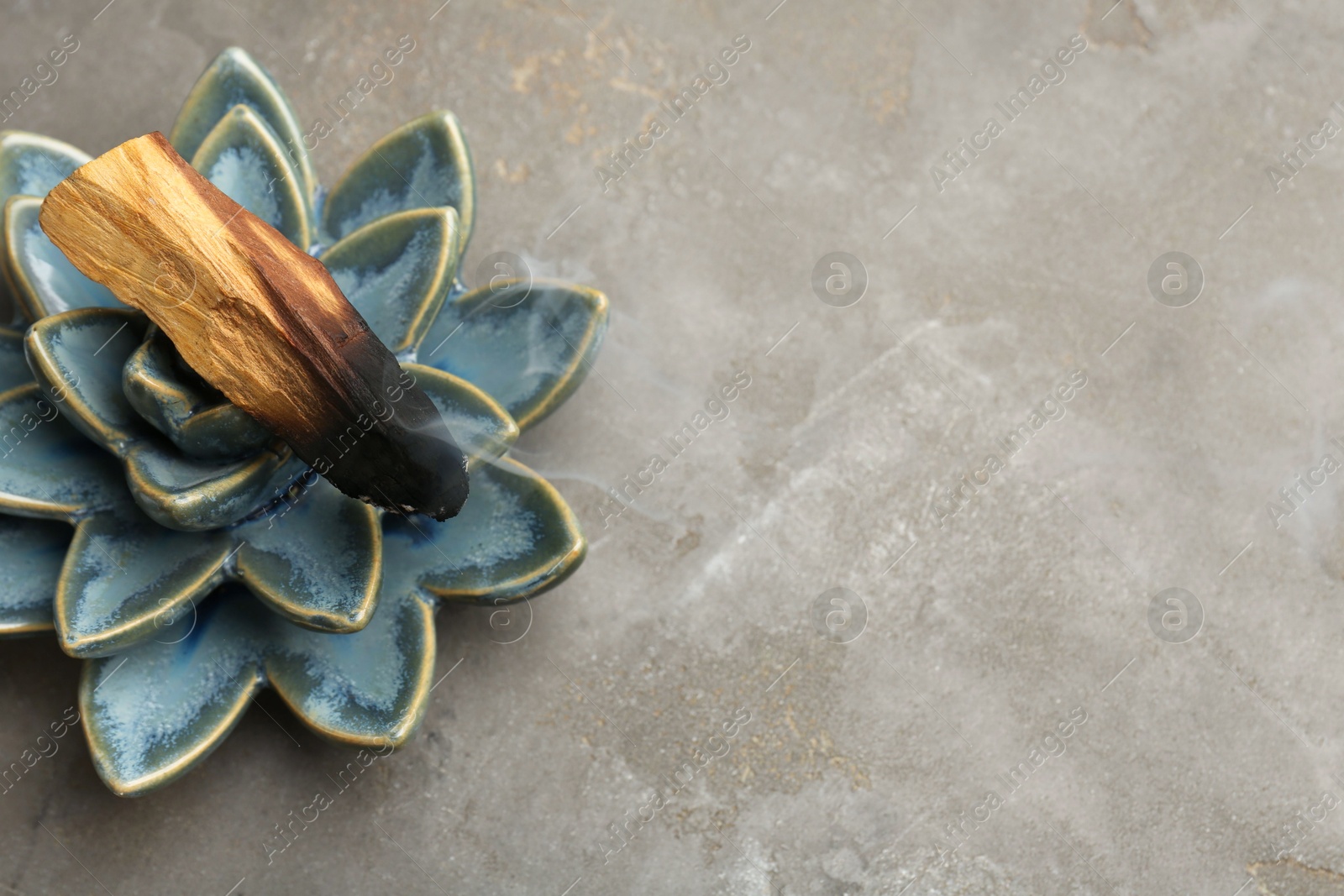 Photo of Smoldering Palo Santo stick and ceramic succulent on gray textured table, closeup. Space for text