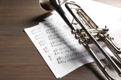 Trumpet and music sheet papers with notes on wooden table, closeup. Space for text