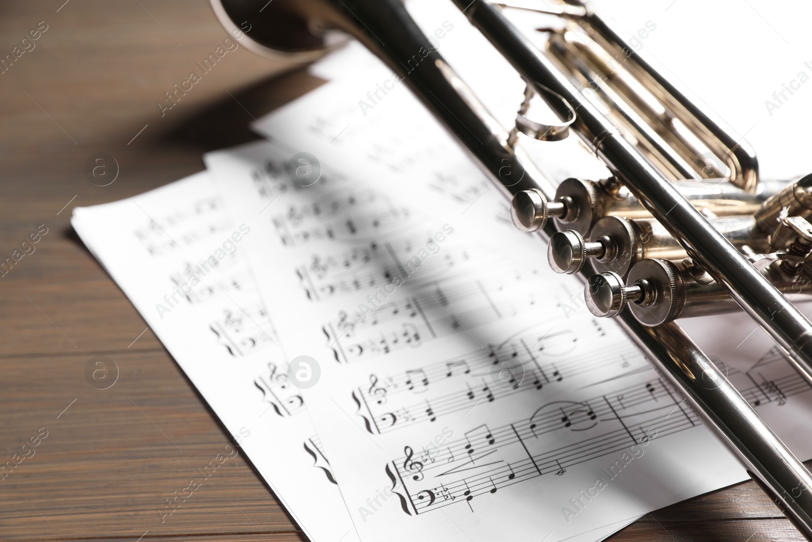 Photo of Trumpet and music sheet papers with notes on wooden table, closeup