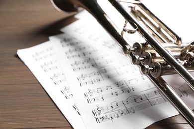 Photo of Trumpet and music sheet papers with notes on wooden table, closeup