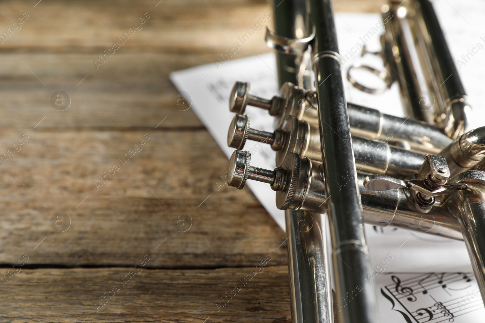 Photo of Trumpet and music sheets on wooden table, closeup. Space for text