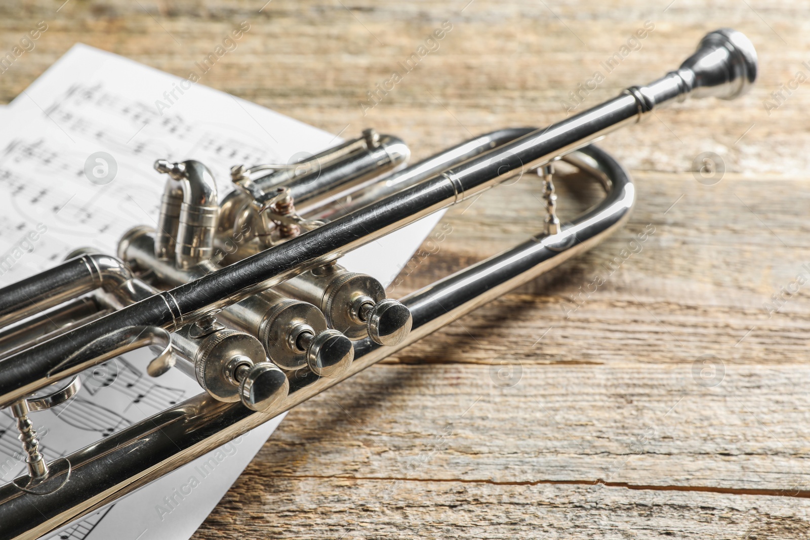 Photo of Trumpet and music sheets on wooden table, closeup