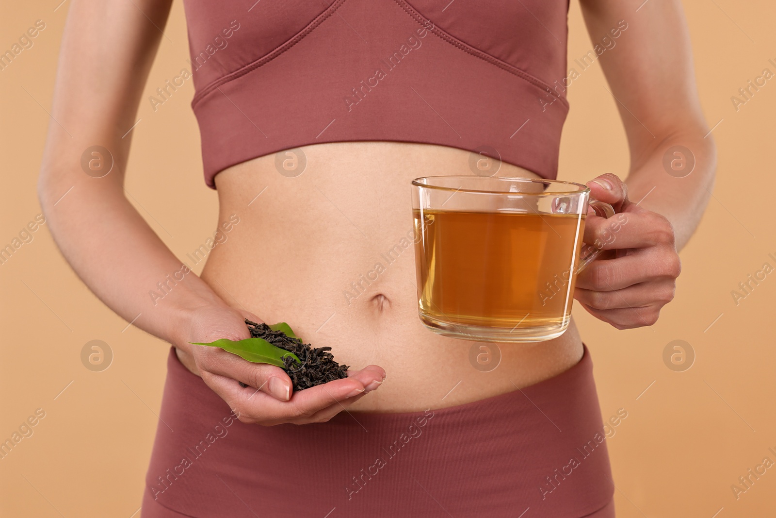 Photo of Weight loss concept. Woman with cup of diet tea and dry leaves on beige background, closeup